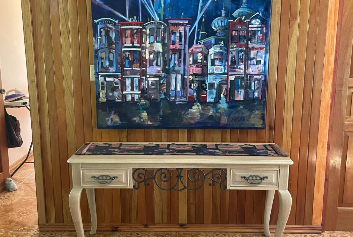 Abstract cityscape painting in blue tones mounted on a wood-paneled wall above a white console table with decorative metalwork.
