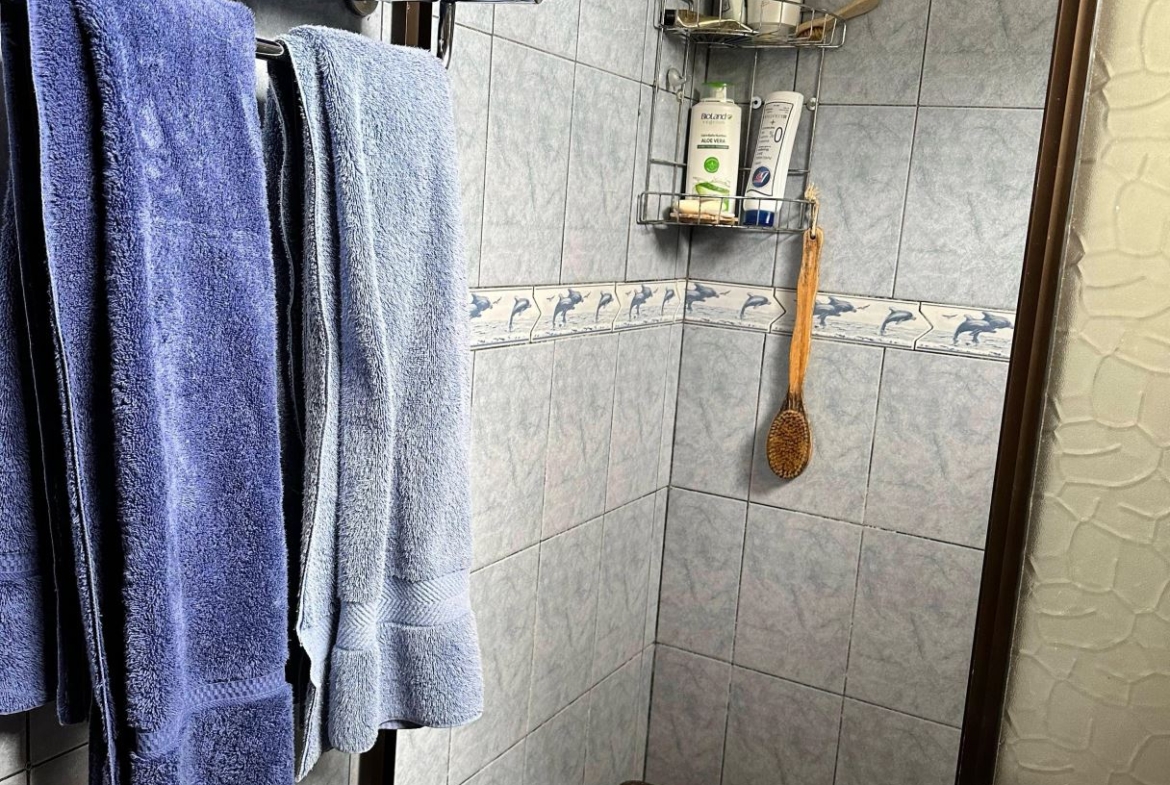 Blue towels hanging on a chrome rack in a blue-tiled bathroom with a small wicker stool beneath.