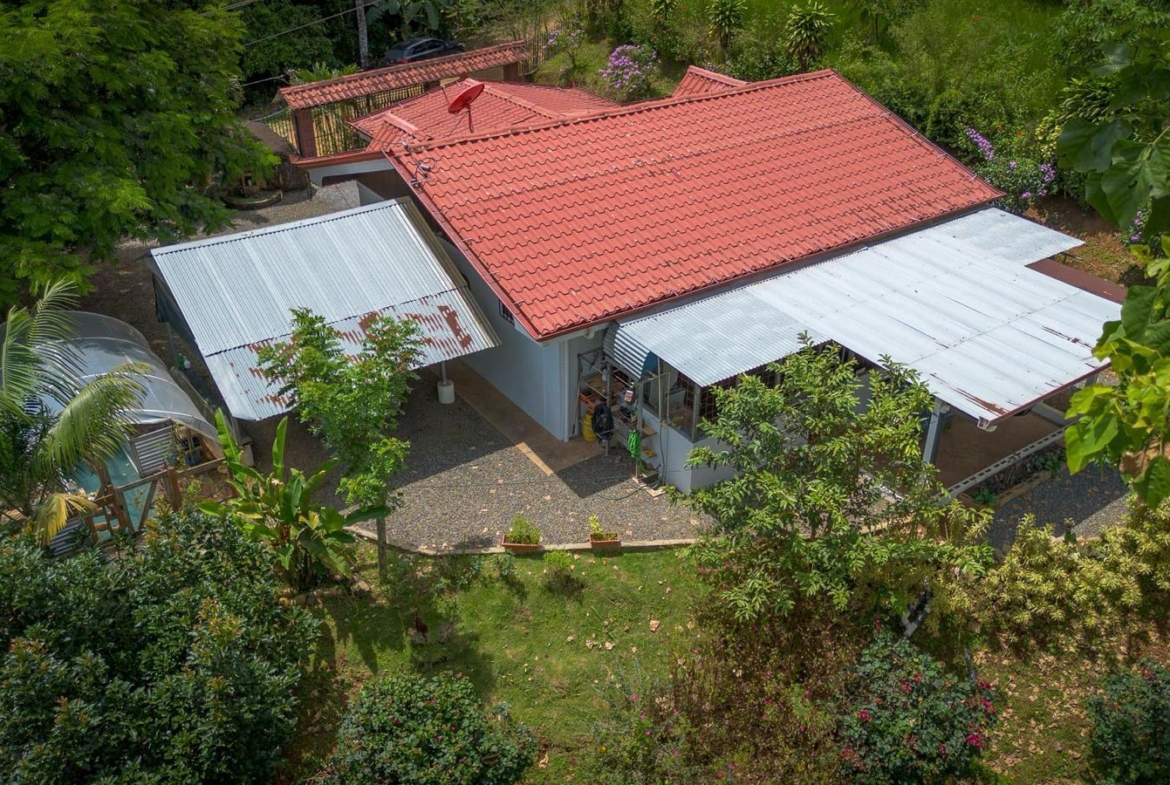 Aerial view of a house with a red tiled roof, metal awnings, and surrounding greenery in a garden setting.