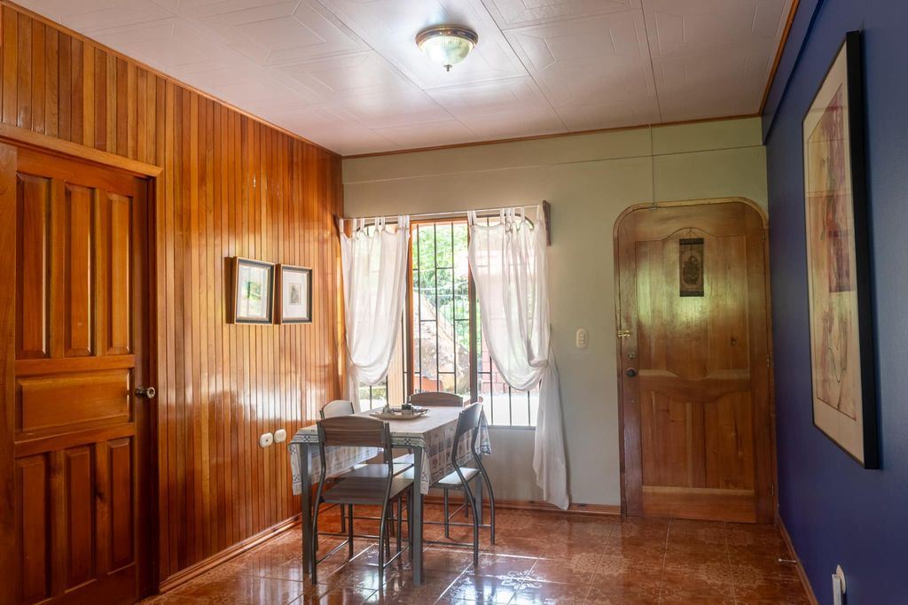 Cozy dining nook with a wood-paneled wall, small table and four chairs by a sunlit window with sheer curtains.