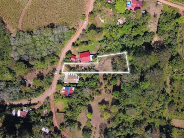 Aerial view of a rural property with a white boundary outline around the main lot, showing a red-roofed building and surrounding trees.
