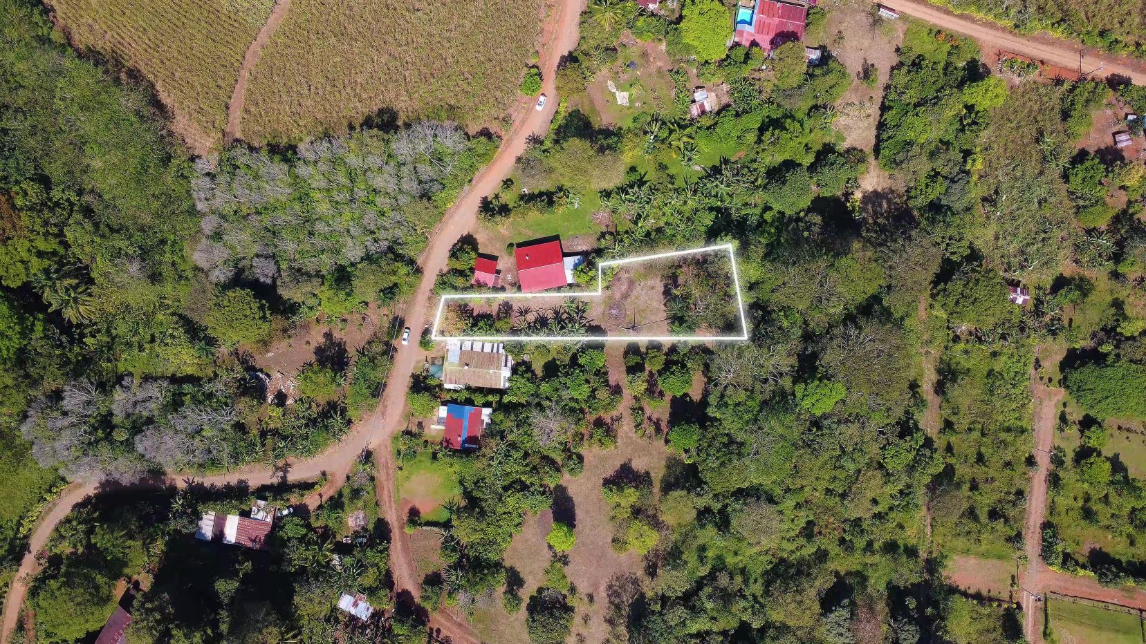 Aerial view of a rural property with a white boundary outline around the main lot, showing a red-roofed building and surrounding trees.