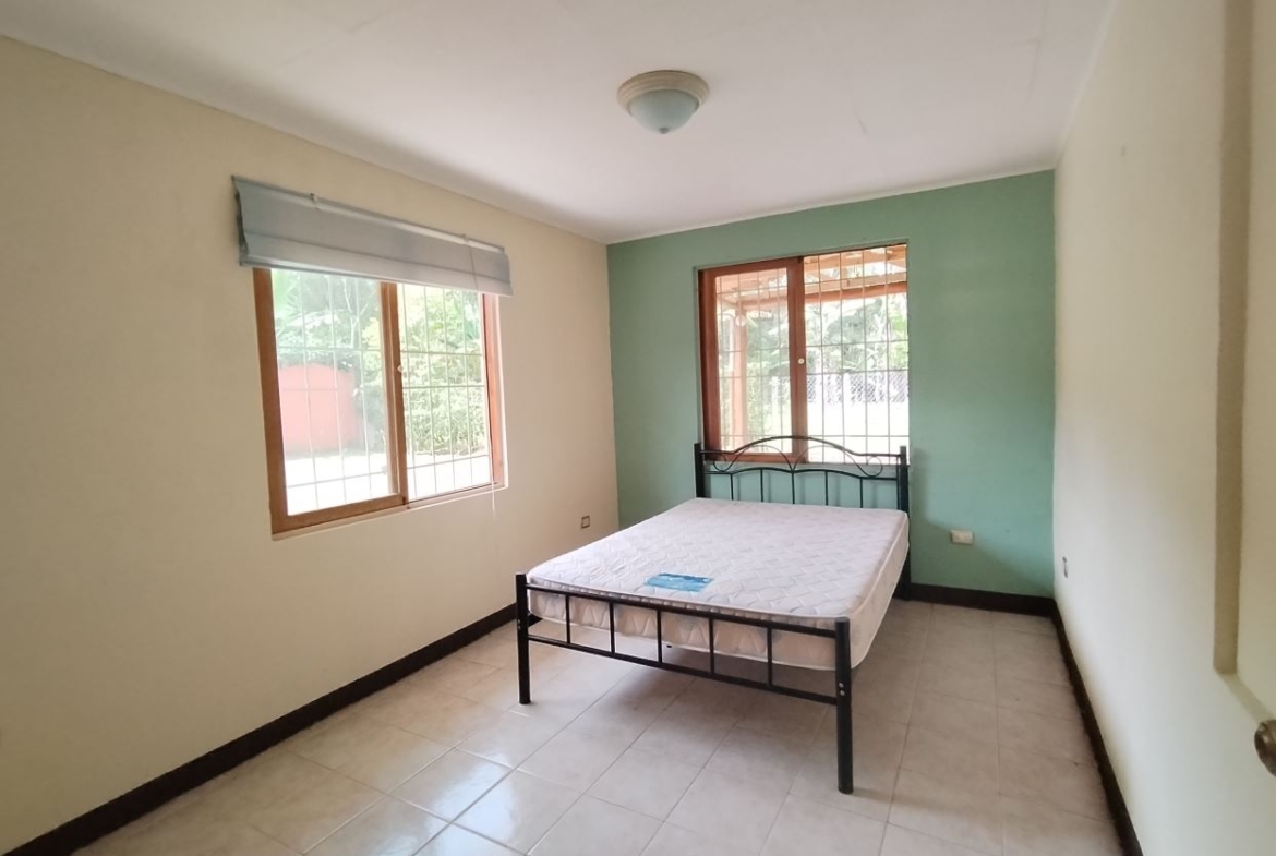 A small bedroom with a metal-framed bed and two windows letting in natural light, one wall painted teal.