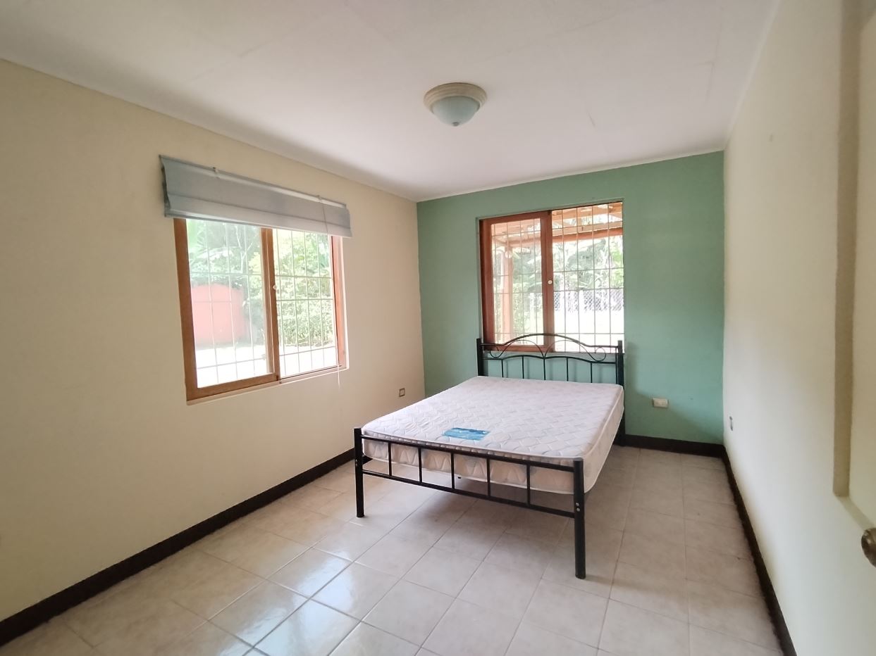A small bedroom with a metal-framed bed and two windows letting in natural light, one wall painted teal.