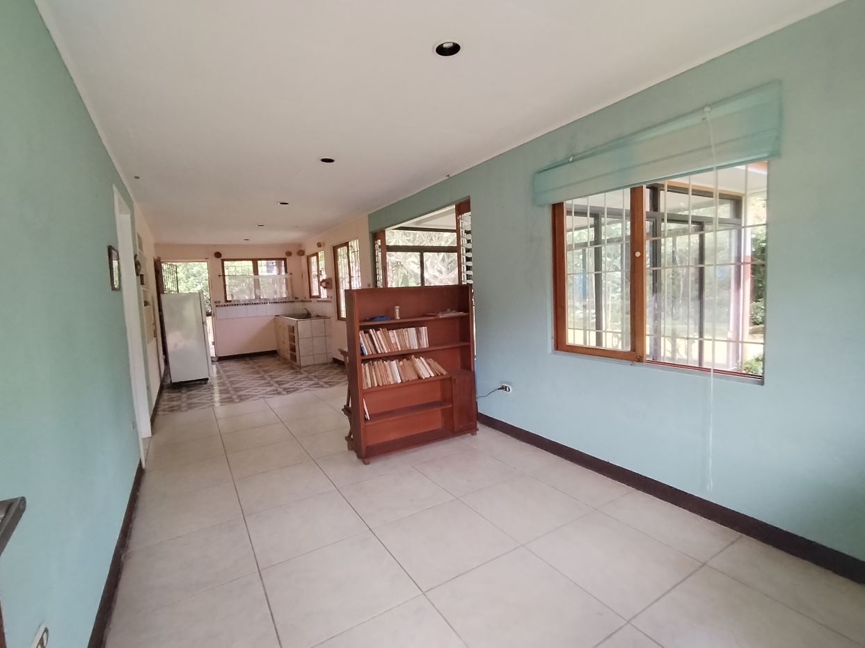 Long bright hallway with light blue walls, tiled floor, and a wooden bookshelf in the middle; large windows along the right wall.]