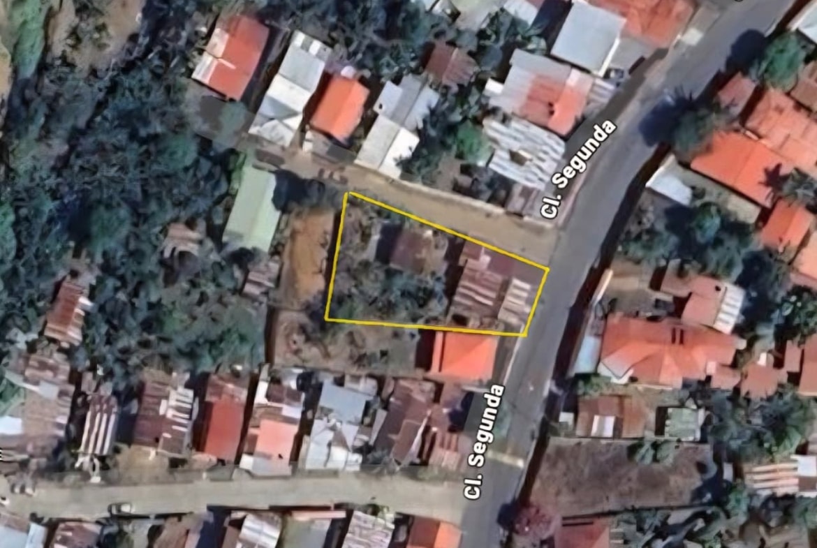 Aerial view of a small residential lot outlined in yellow at the corner of Cl. Segunda, surrounded by houses and trees.