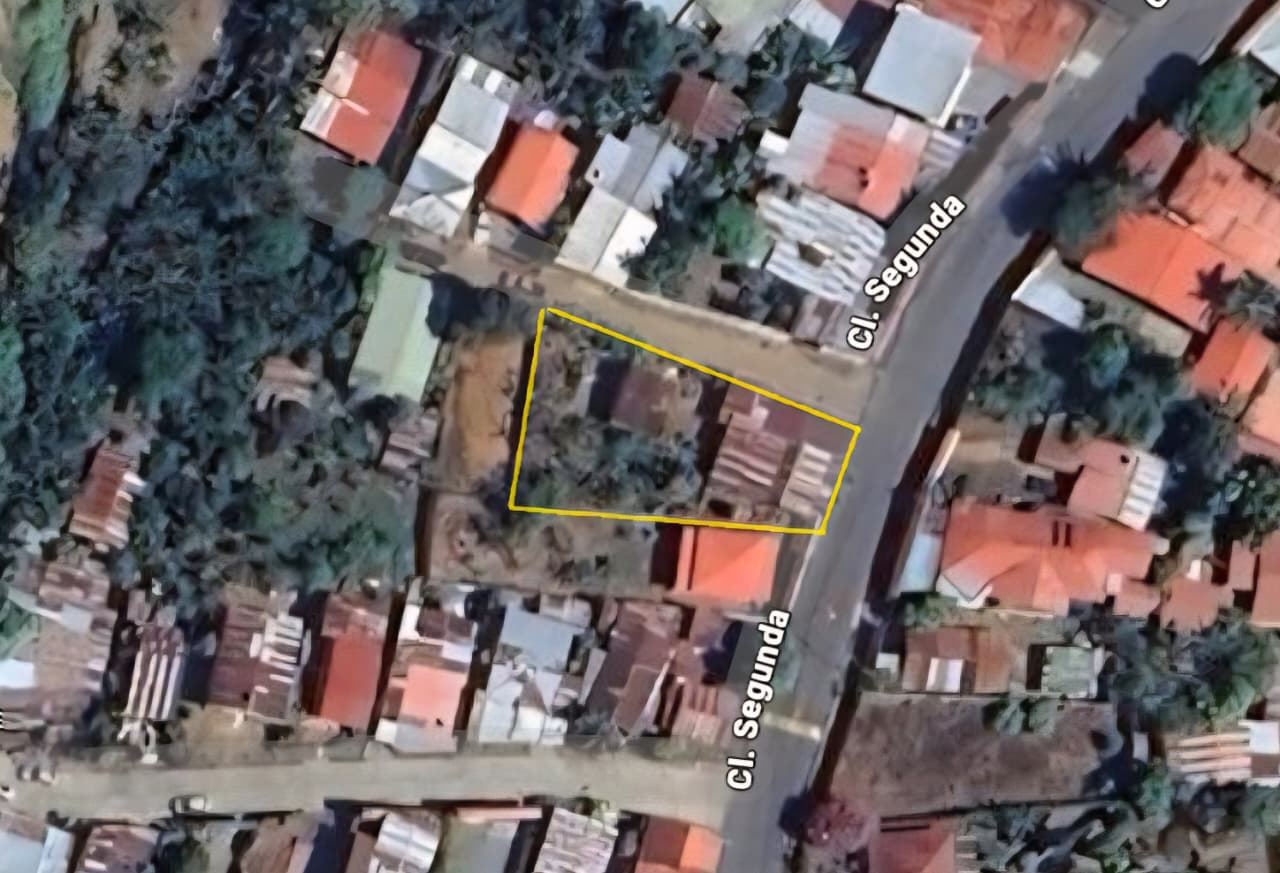 Aerial view of a small residential lot outlined in yellow at the corner of Cl. Segunda, surrounded by houses and trees.