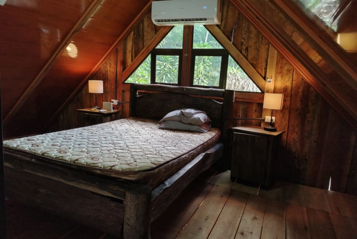 A rustic bedroom with a wooden bed, two nightstands, and an overhead air conditioner in a sloped-ceiling cabin windowed room