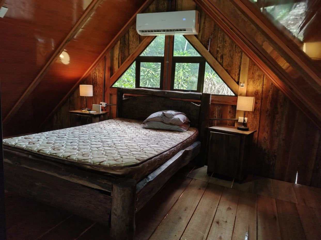 A rustic bedroom with a wooden bed, two nightstands, and an overhead air conditioner in a sloped-ceiling cabin windowed room