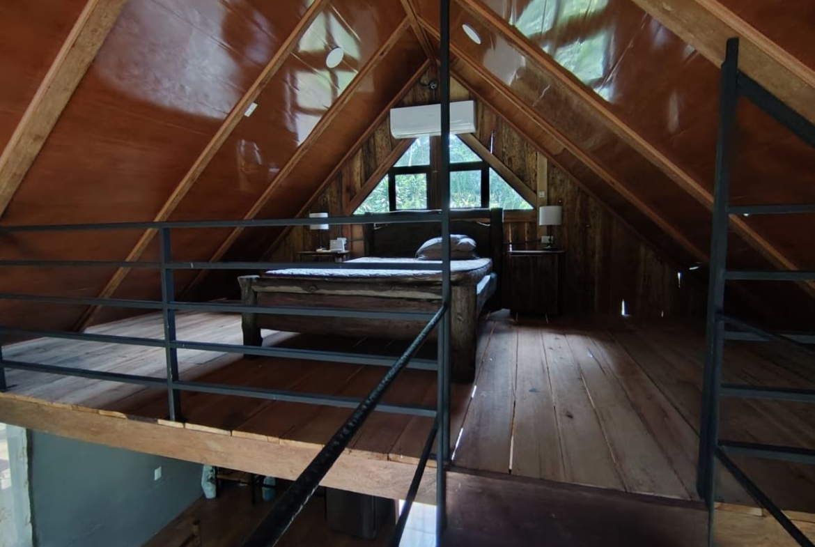 A rustic attic bedroom in an A-frame cabin with exposed wood walls, a bed against the back wall, and two small nightstands under a sloped ceiling.