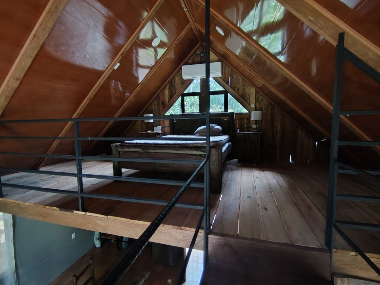 A rustic attic bedroom in an A-frame cabin with exposed wood walls, a bed against the back wall, and two small nightstands under a sloped ceiling.