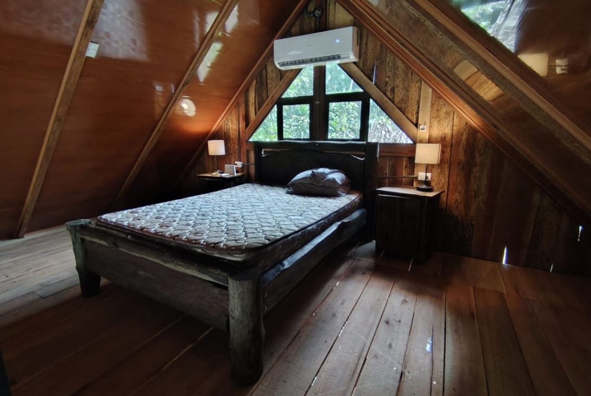 Rustic attic bedroom with a wooden bed, two nightstands, lamps, and a triangular windowed wall.
