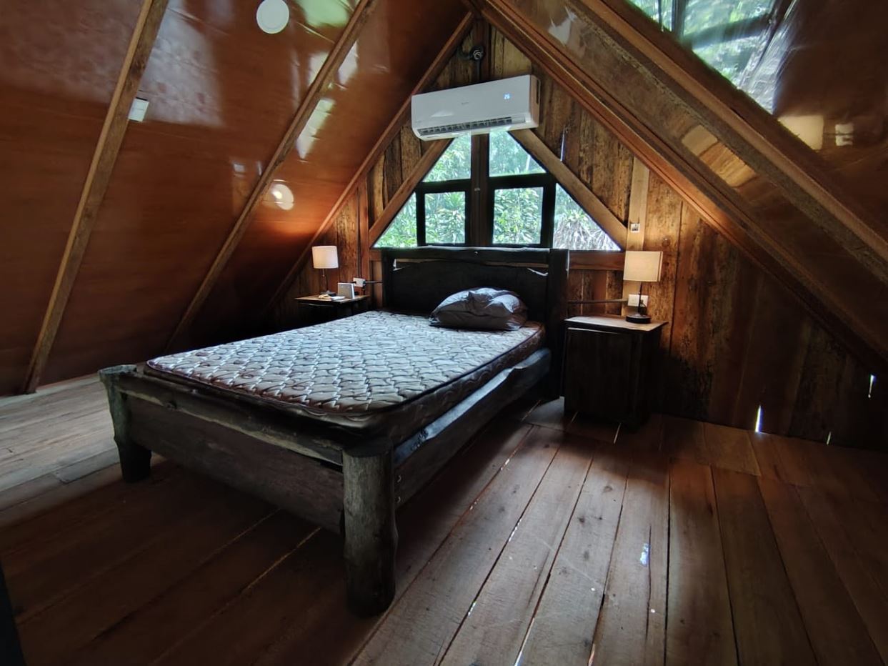 Rustic attic bedroom with a wooden bed, two nightstands, lamps, and a triangular windowed wall.