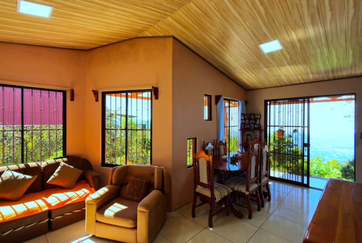 Open living-dining area with beige sofa set and wooden dining table, large windows and doors revealing a sea view.