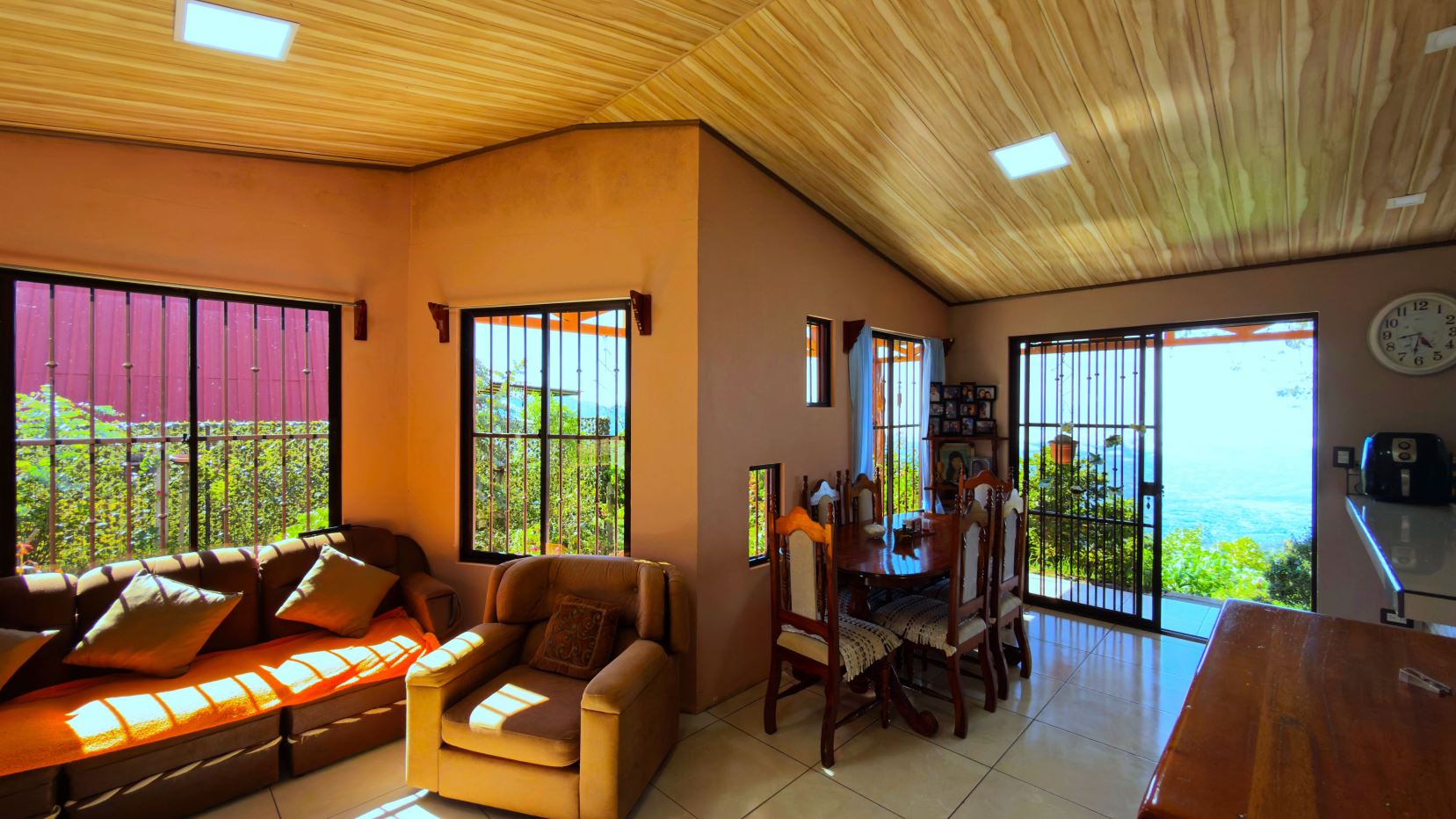 Open living-dining area with beige sofa set and wooden dining table, large windows and doors revealing a sea view.