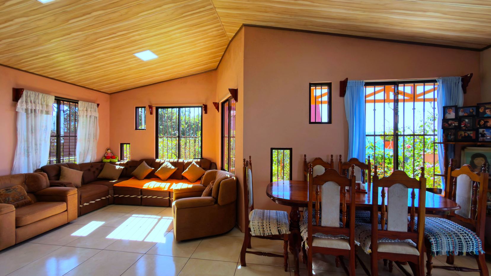 Bright living room with peach walls, wooden ceiling, and a tan sectional sofa arranged around a coffee table area.