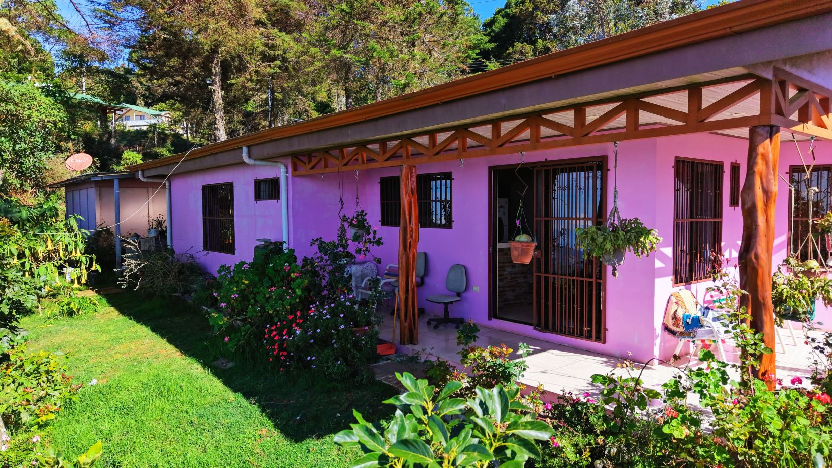 Pink single-story house with a covered porch and hanging plants in a lush garden.