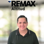 Portrait of a smiling man in a black polo shirt with the REMAX Altitud logo in the blurred background behind him.