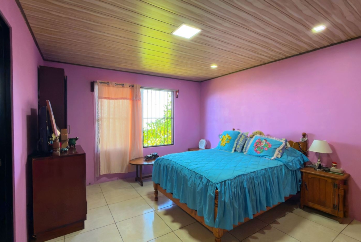 Bedroom with pink walls and blue bedspread; window with sheer curtains beside a wooden bed.