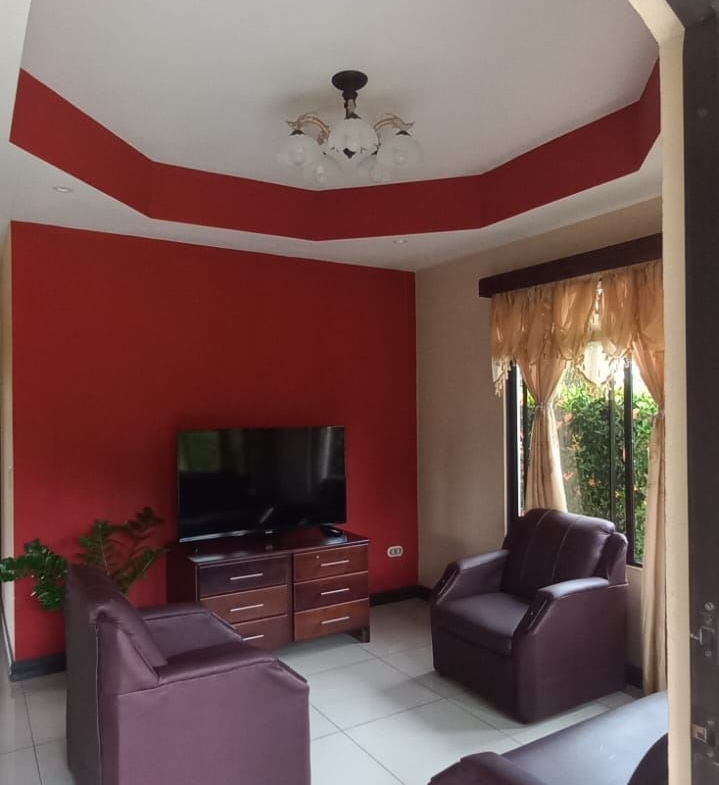 Living room with red accent wall, white tile floor, and four purple armchairs around a wooden TV console with a flat-screen TV.