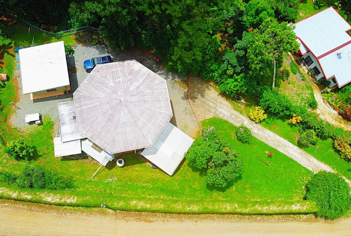 Aerial view of a property with a large octagonal-roof building, white sheds, and lush green landscaping along a water edge.