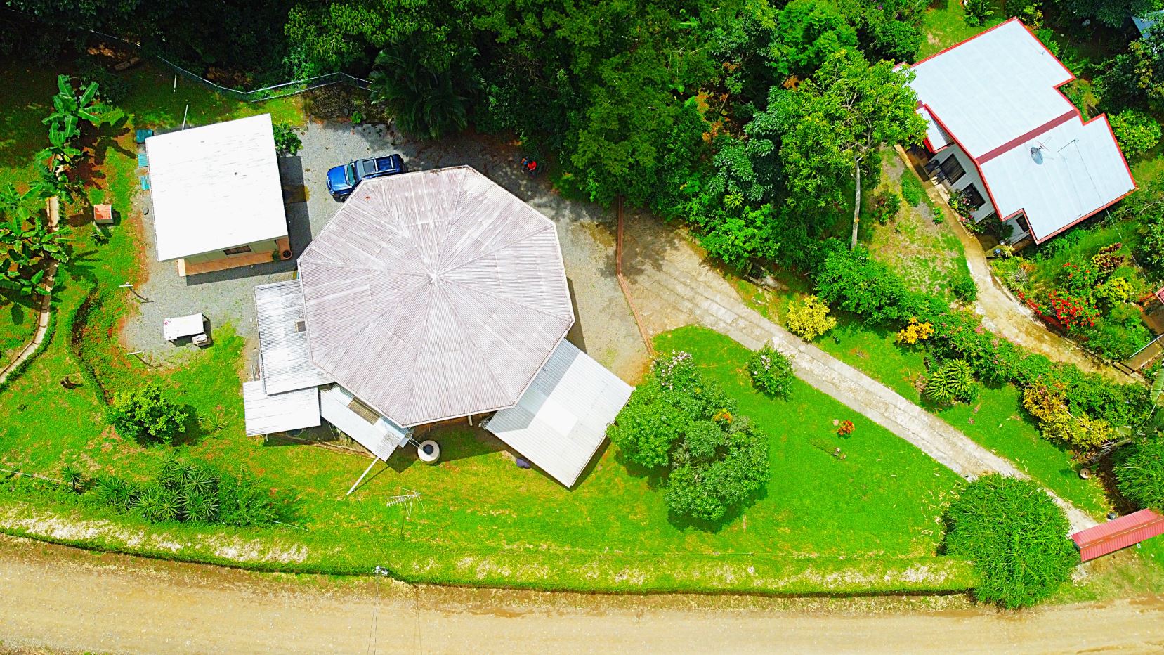 Aerial view of a property with a large octagonal-roof building, white sheds, and lush green landscaping along a water edge.