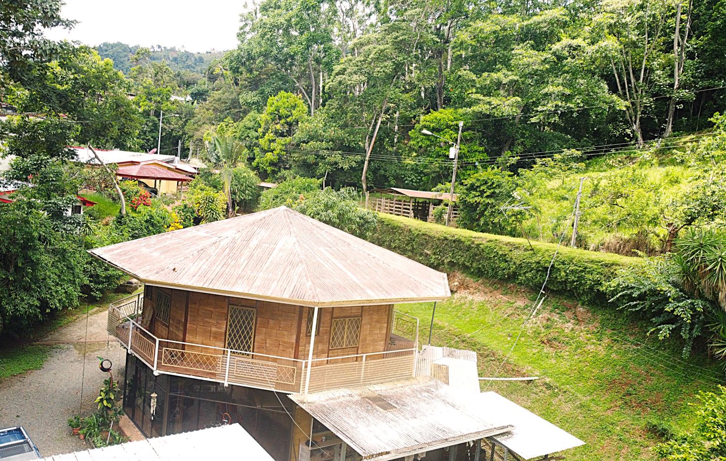 Wooden house with a wraparound balcony on a grassy hillside, surrounded by dense tropical trees.