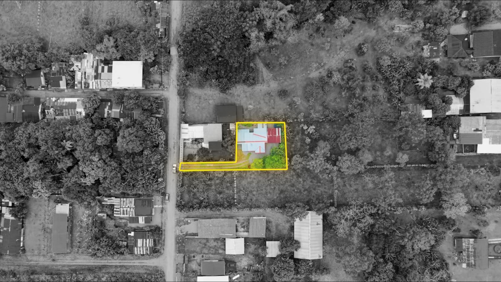 Aerial view of a house with a blue and red roof inside a yellow-outlined lot, with a small garden and surrounding trees in a suburban area.