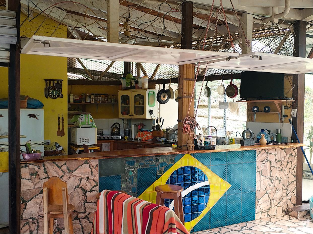Open-air kitchen/bar with a mosaic Brazilian flag on the counter front and hanging pots above the bar