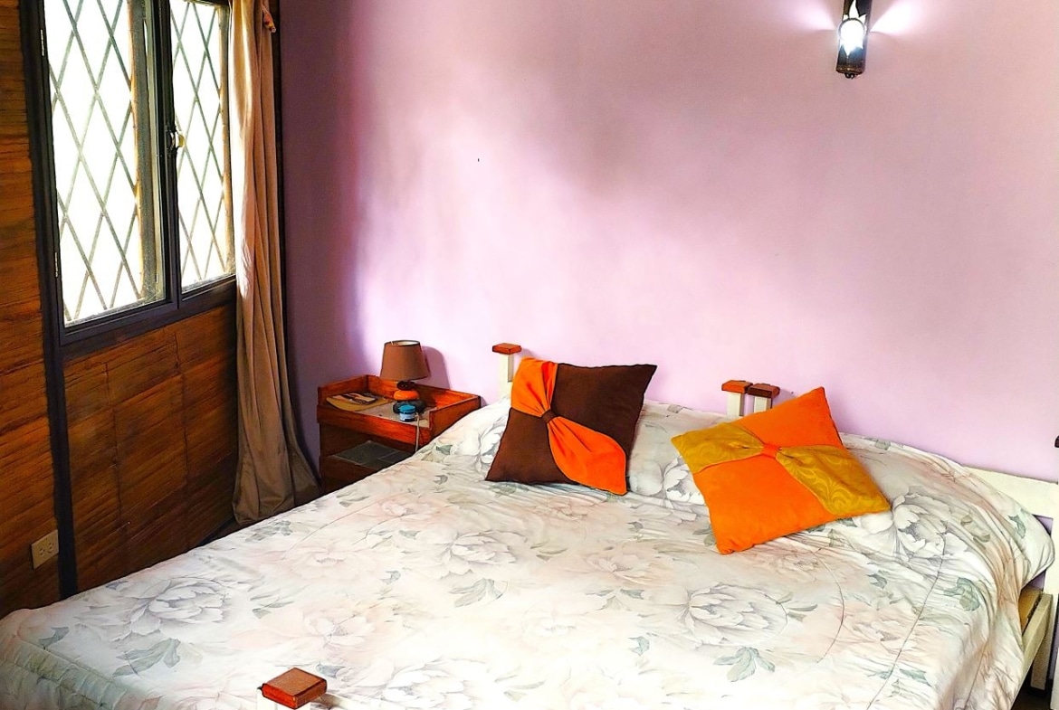 Cozy bedroom with a pink wall, a large bed covered in a floral quilt, and orange-brown and orange pillows beside wooden bedside tables.