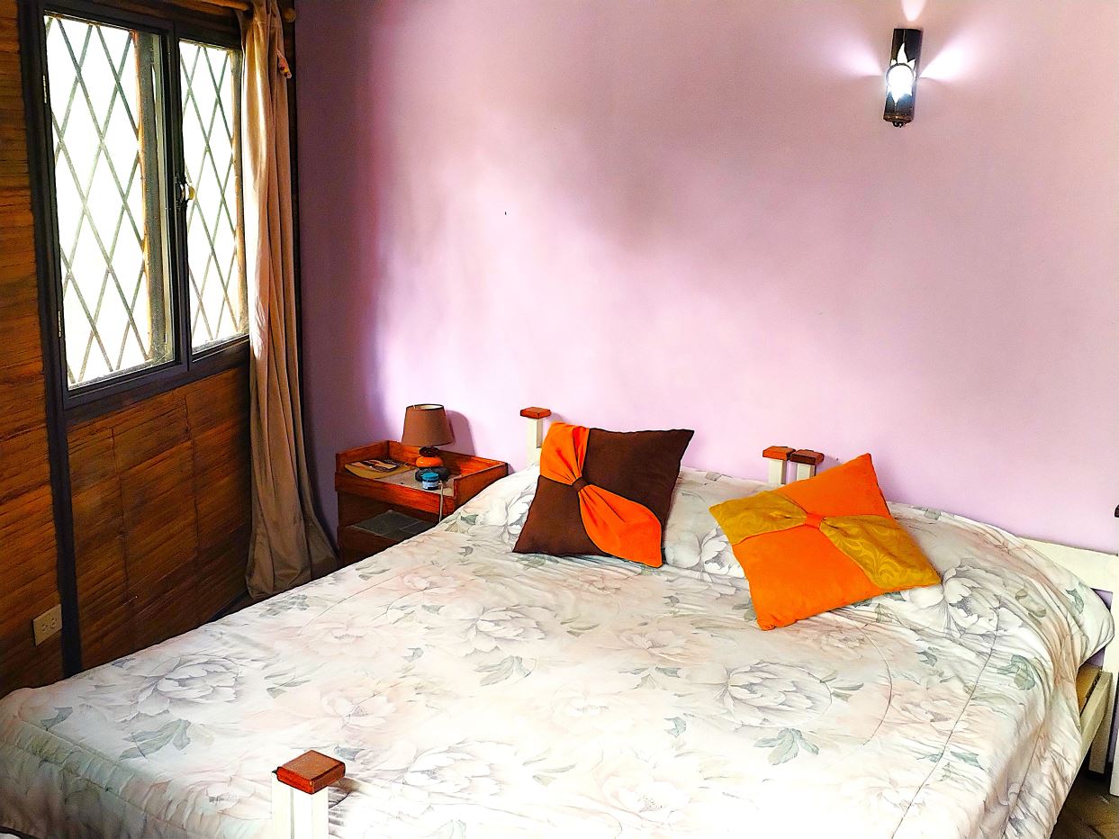 Cozy bedroom with a pink wall, a large bed covered in a floral quilt, and orange-brown and orange pillows beside wooden bedside tables.