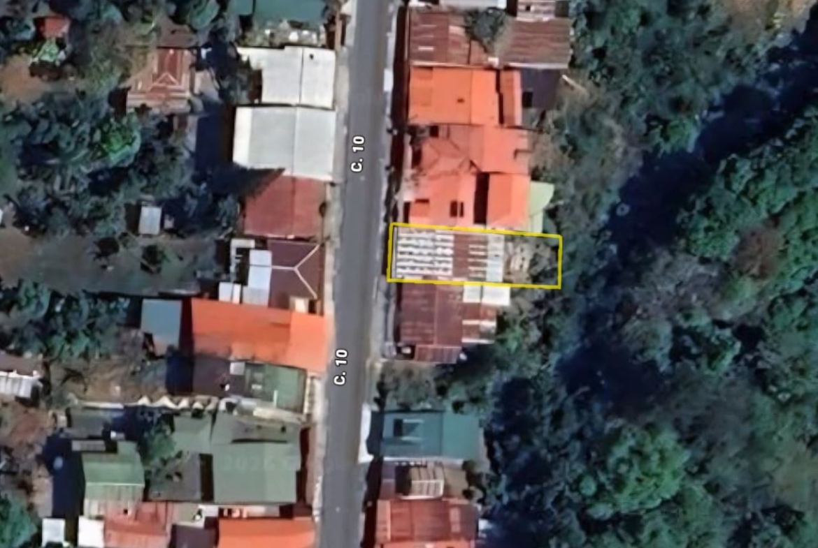 Aerial view of a narrow street with colorful rooftops; a yellow rectangle marks a two-story building on the right side of the road.