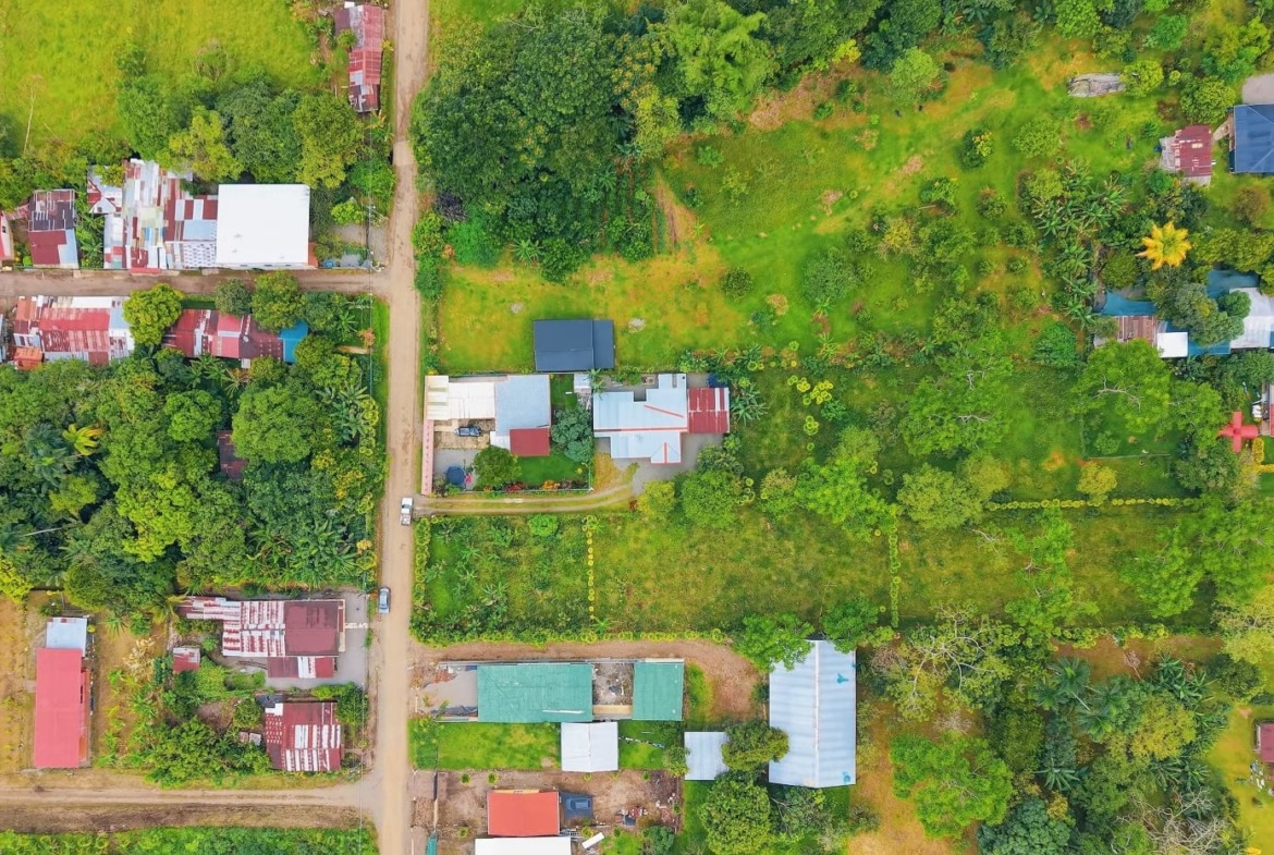Aerial view of a village with red-roofed houses along dirt streets amid dense green trees and open grassy plots.