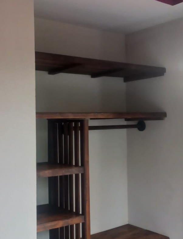 Open wooden closet with vertical slatted divider, two shelves, a hanging rod, and a lower bench in a neutral-toned bedroom corner.