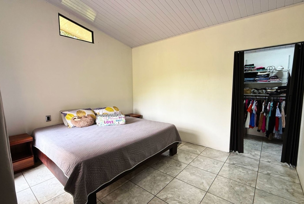 Bedroom with a queen bed, gray quilt, two wooden nightstands, and an open closet on the right showing clothes.