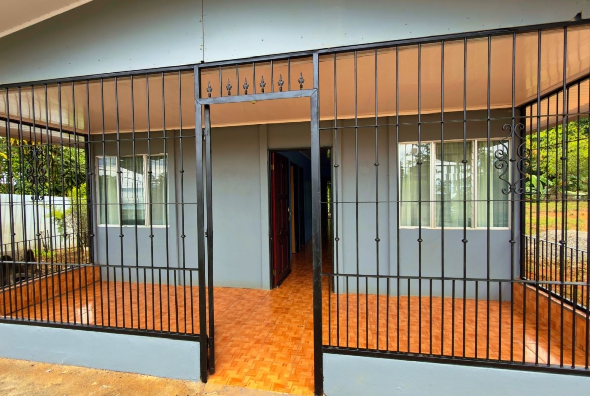 Front of a house with a black iron fence and gate, orange tiled porch, and an open doorway into the interior.