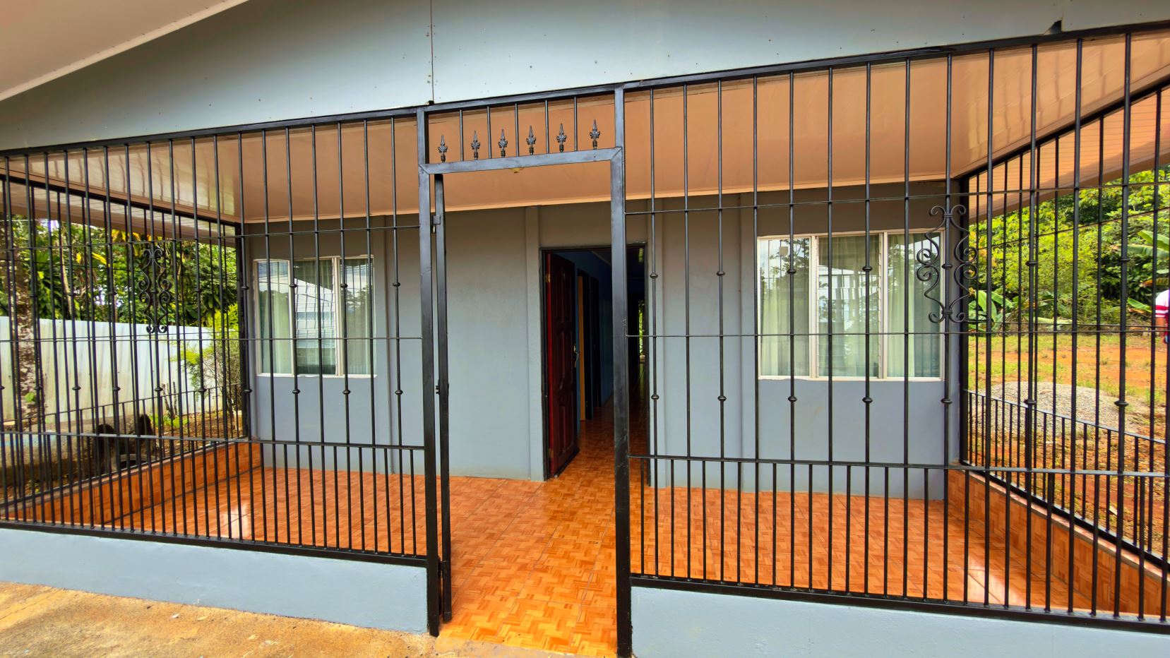 Front of a house with a black iron fence and gate, orange tiled porch, and an open doorway into the interior.