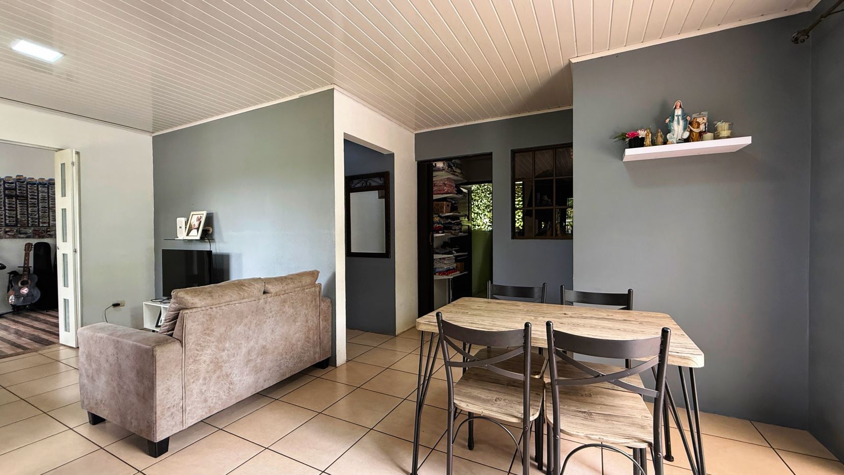 Open-plan living and dining area with beige sofa, TV stand, and framed photo against blue-gray walls; wooden dining table and six chairs nearby.