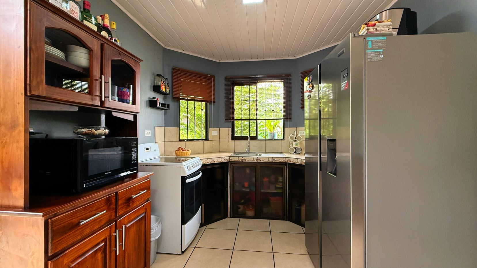 Cozy kitchen with dark wood cabinets, white appliances, and two windows with wooden blinds.