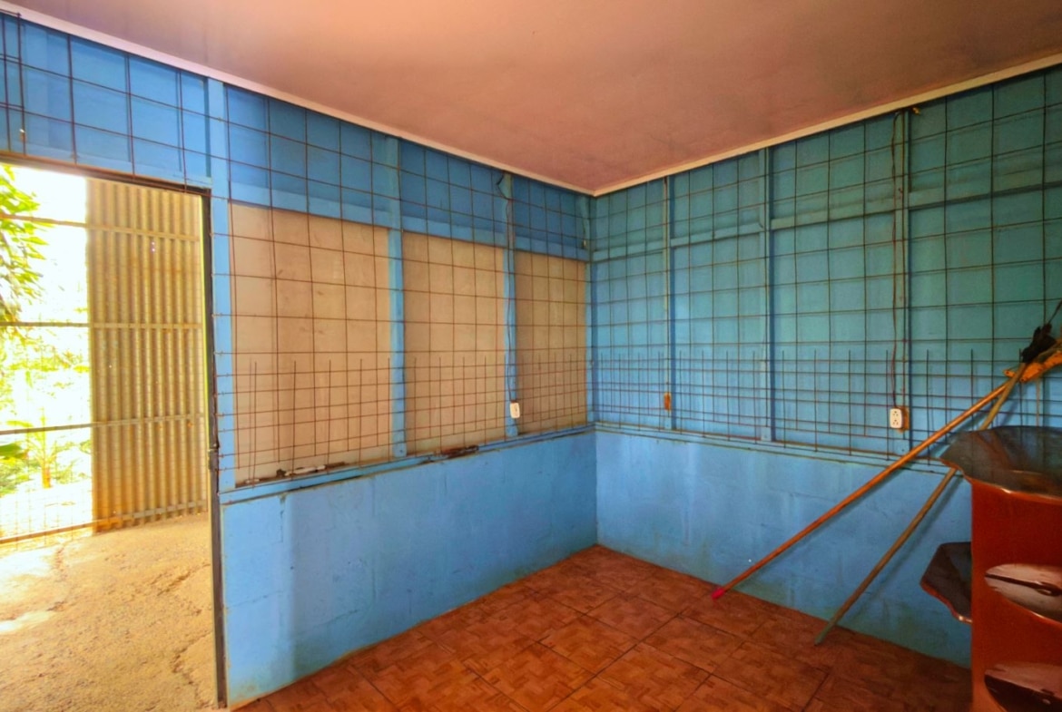 Blue tiled room with metal grid wall panels, a mop leaning on a wooden shelf, and an open door to a sunlit outdoor area.