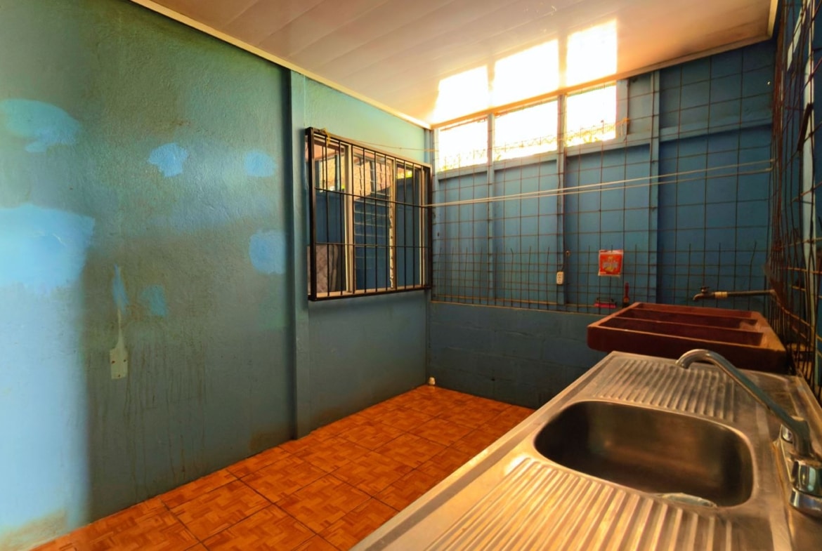 Blue utility room with stainless steel sink in foreground, blue walls, and orange tiled floor. Windows with bars along the back wall.