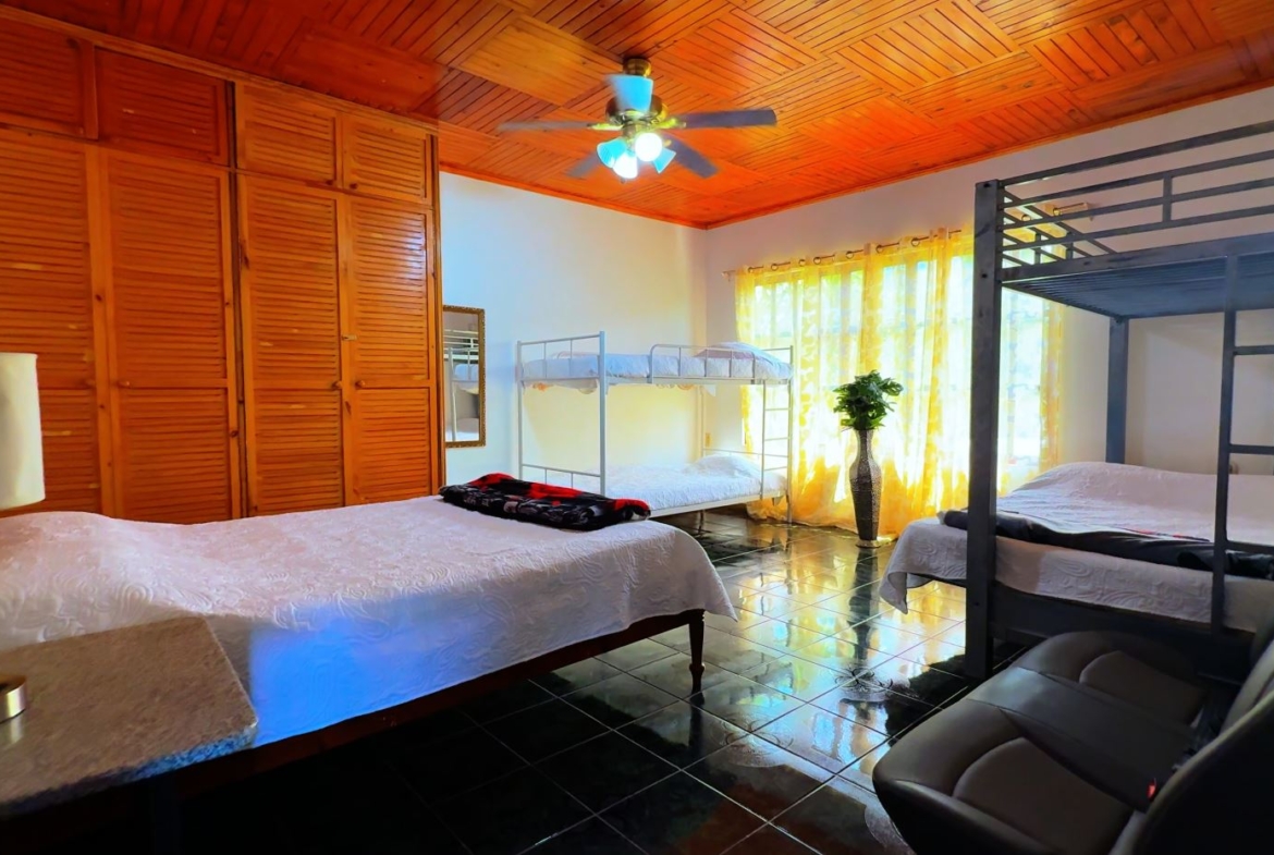 Bedroom with wooden paneled ceiling, large wardrobe, two bunk beds and a single bed under a window with yellow curtains