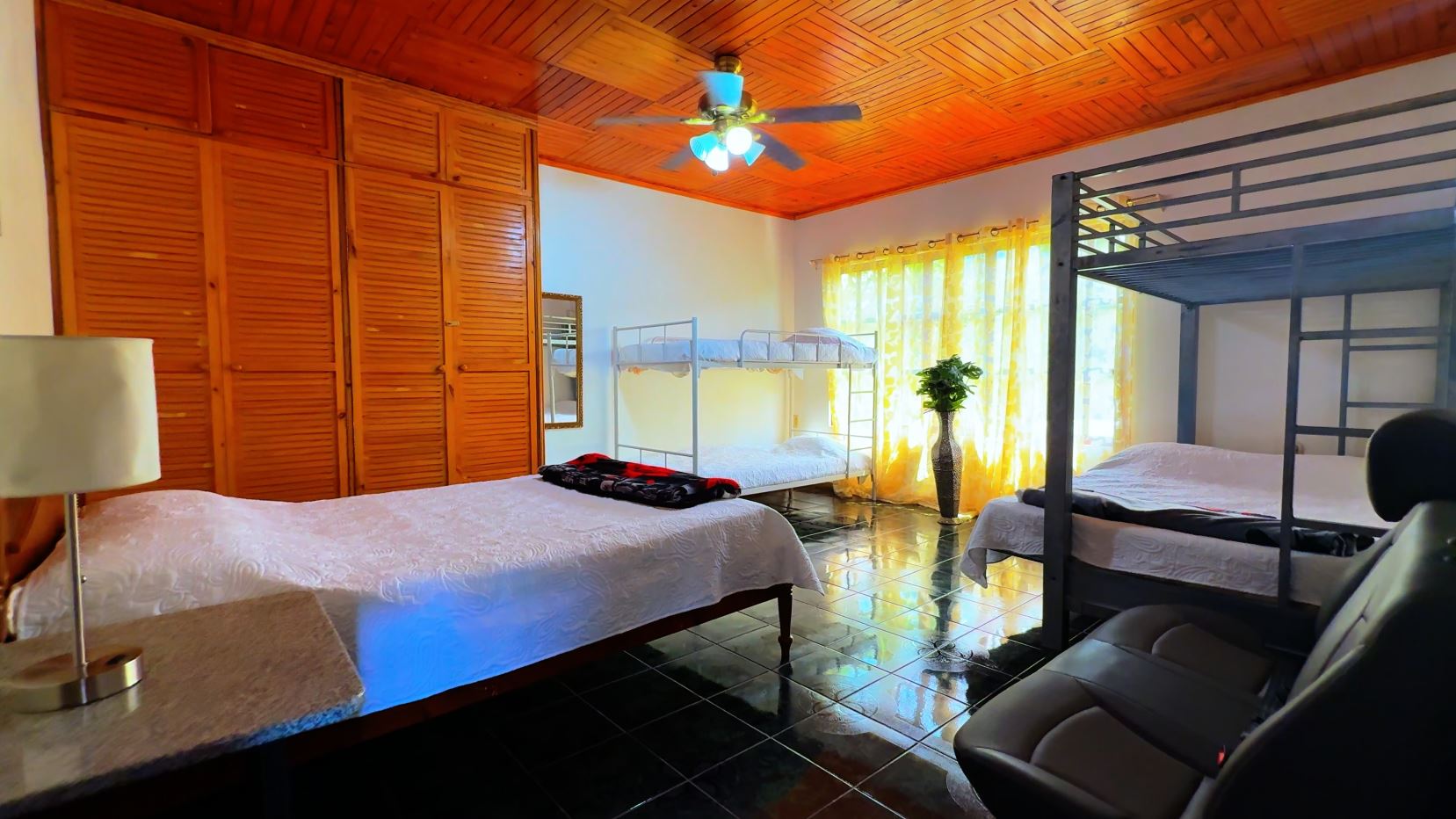 Bedroom with wooden paneled ceiling, large wardrobe, two bunk beds and a single bed under a window with yellow curtains