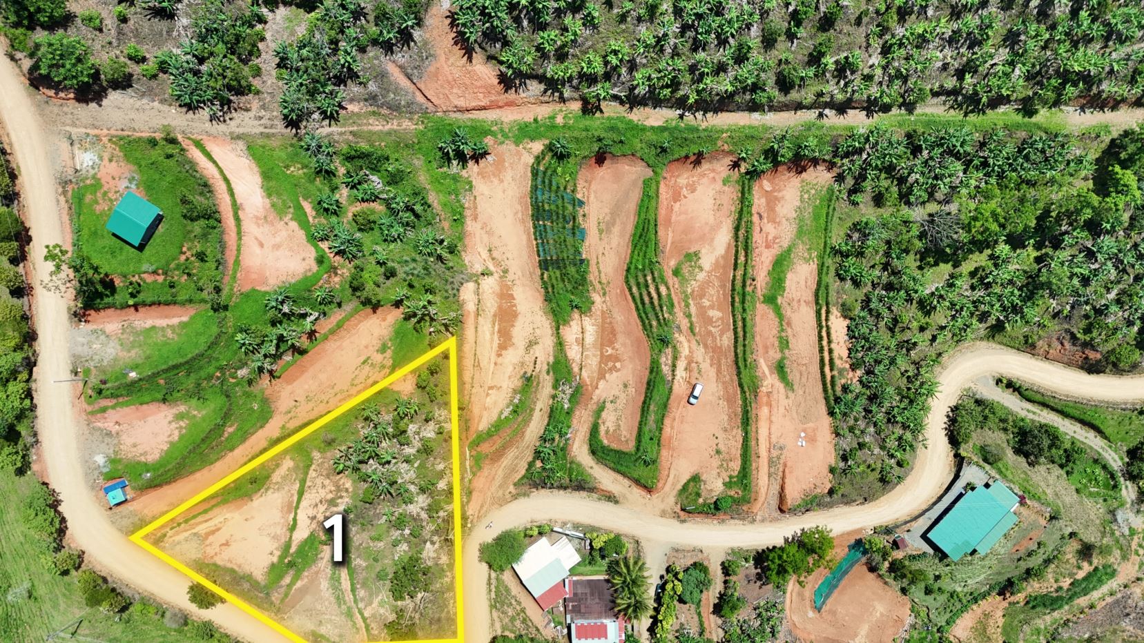 Aerial view of a farmland plot with a yellow-outlined triangle labeled '1' along a dirt road. Vegetation and small buildings surround the area.