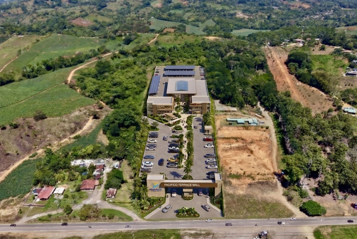 Aerial view of Pacifico Terrace Mall in a green hillside setting with a large parking lot and solar panels on the roof.