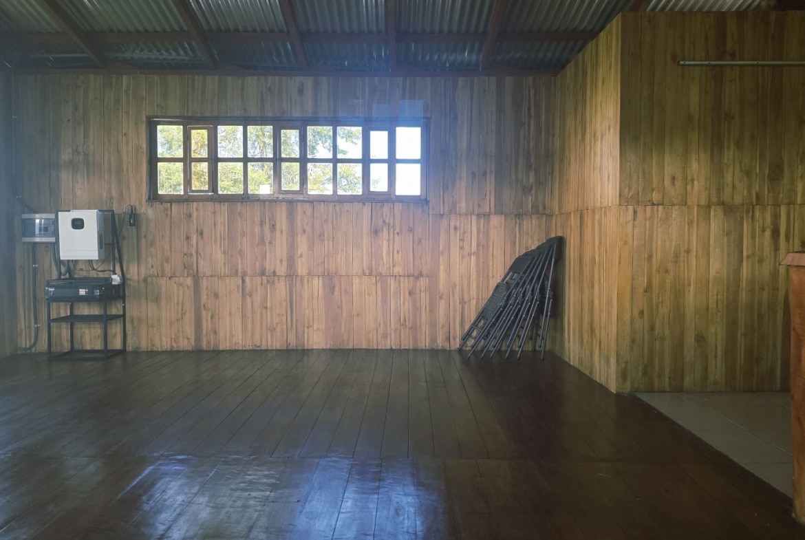 Empty wooden-paneled room with a row of small windows, and a few folding chairs stacked against the right wall near a table with equipment left of center