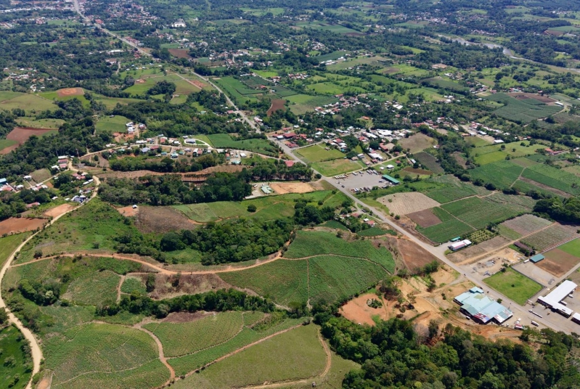 Aerial view of a rural landscape with patchwork fields, trees, and a small town connected by roads from above.