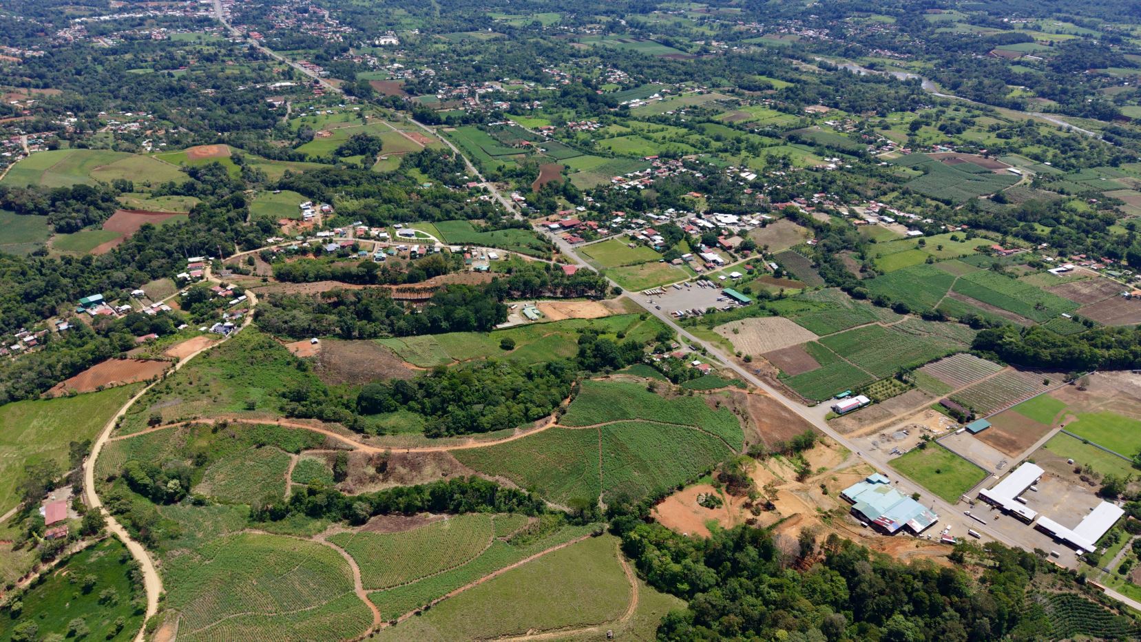 Aerial view of a rural landscape with patchwork fields, trees, and a small town connected by roads from above.