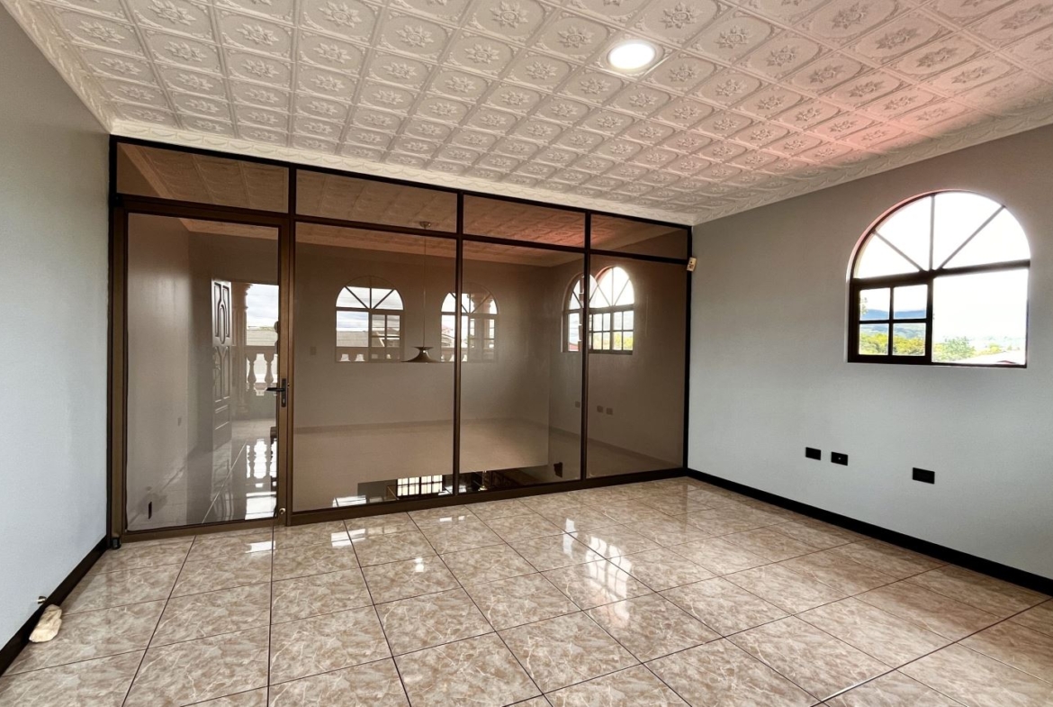 Empty office or living room with marble-tile floor, glass-framed partition and arched window, neutral walls, and decorative patterned ceiling paneling