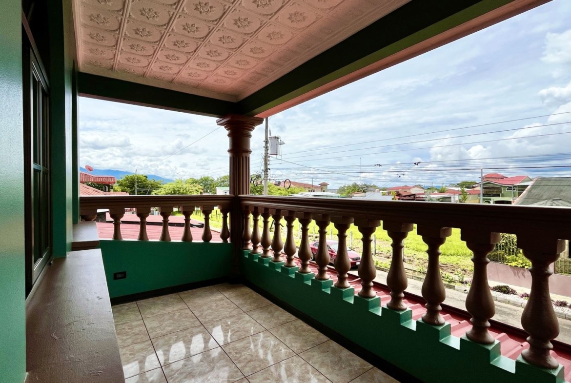 Green-painted balcony with brown decorative balusters and tiled floor, overlooking a suburban street.